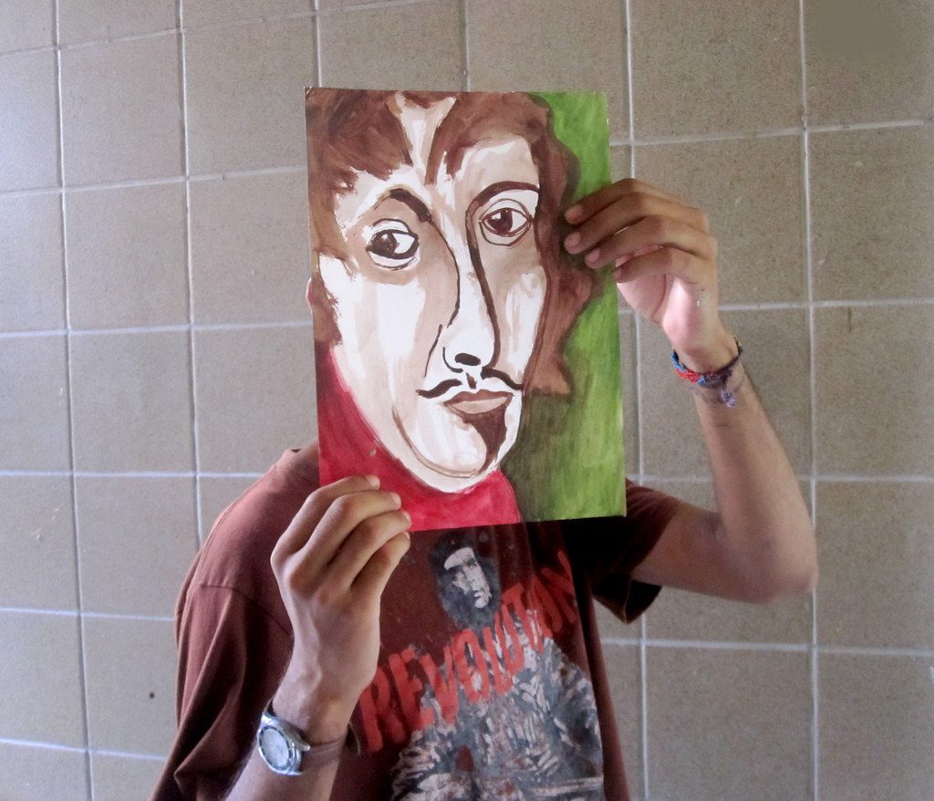 Rodrigo Palhares segurando uma de suas pinturas diante do rosto